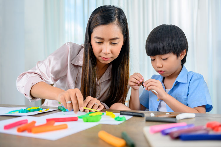 asian woman and boy working together with craft and writing supplies